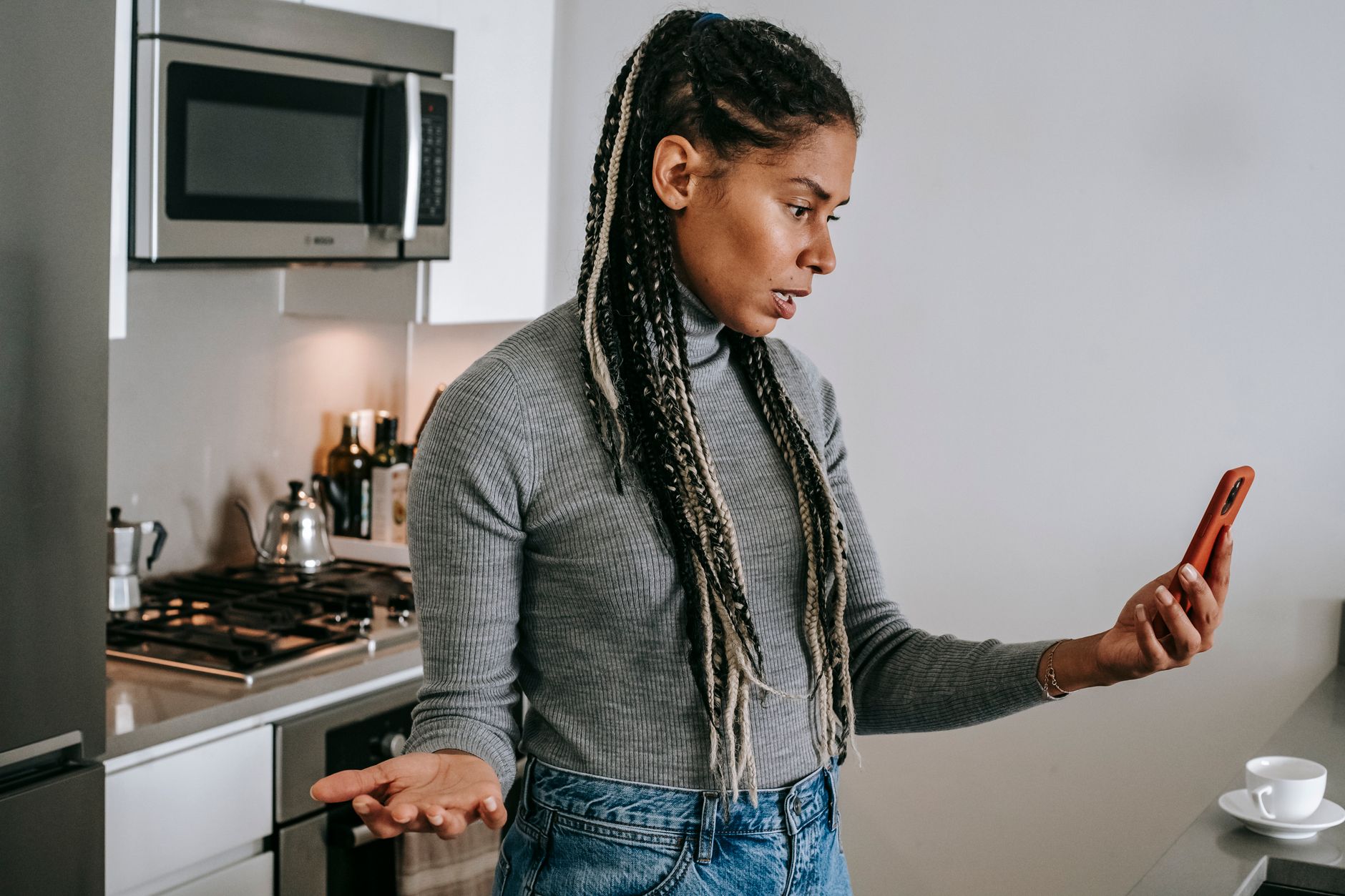 mulher olhando o celular com expressão preocupada em uma cozinha
