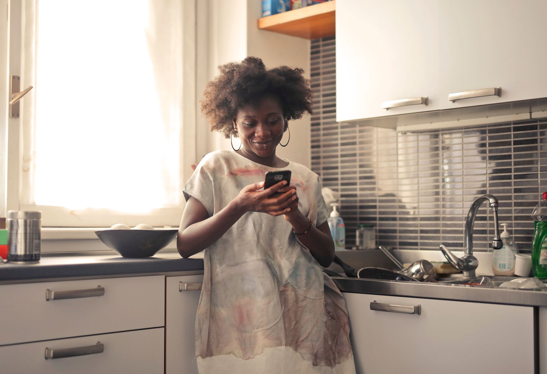 mulher digitando no celular apoiada na bancada da cozinha